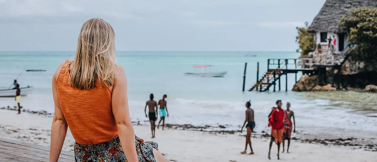 Kobieta patrzy na plażę z Zanzibar, gdzie widać łodzie, ludzi i charakterystyczne atrakcje wyspy.