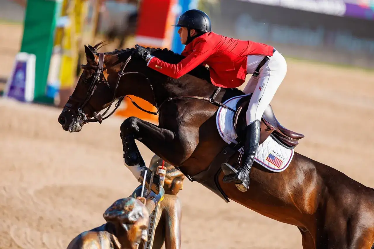 Le cheval Balou du Reventon saute un obstacle avec son cavalier en tenue rouge et blanche.