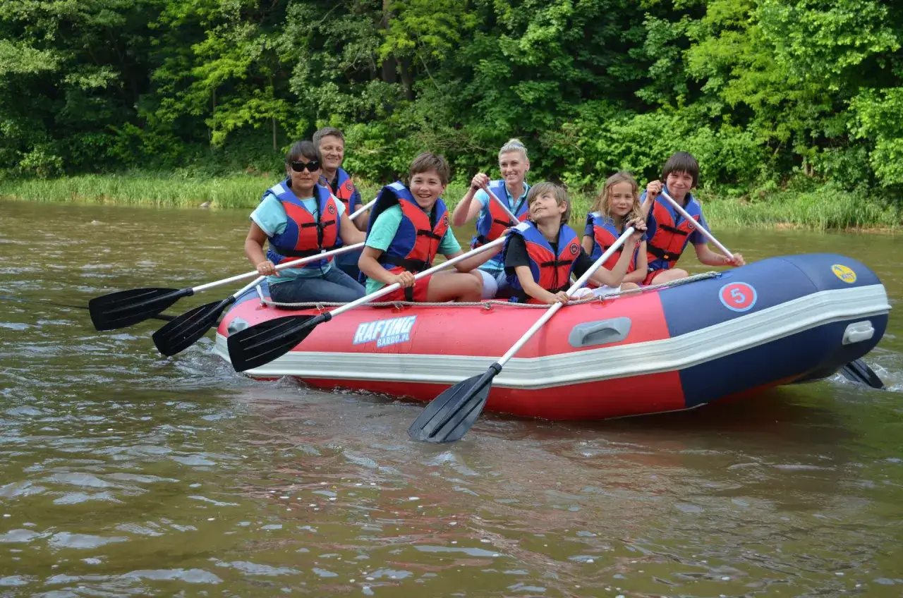 Grupa ludzi na pontonie, wiosłująca po rzece. To jest właśnie rafting – wodna przygoda!