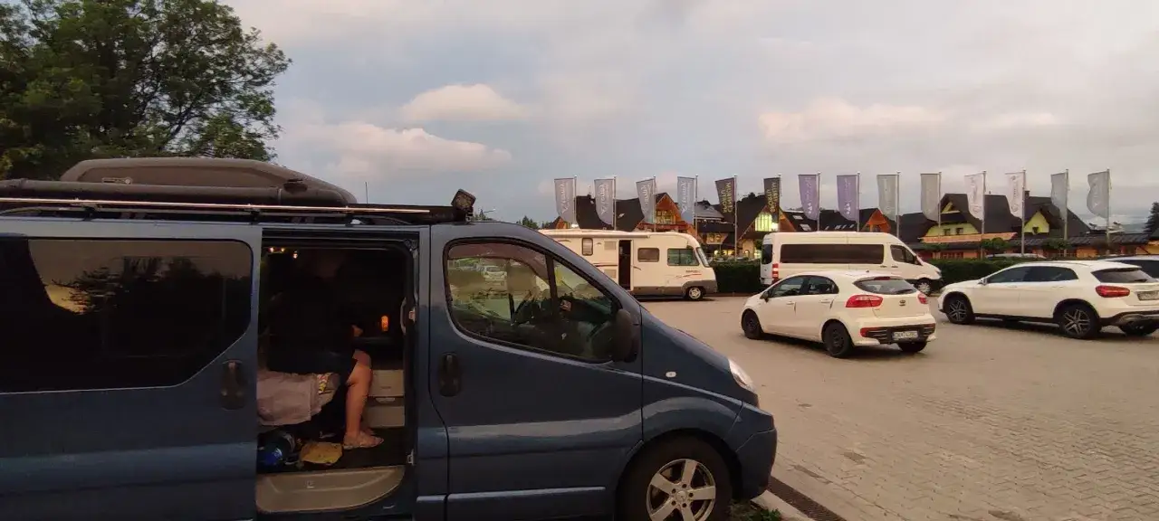 Na parkingu przy Chochołowskich Termach stoi ciemnoniebieski bus, biały samochód i kamper.