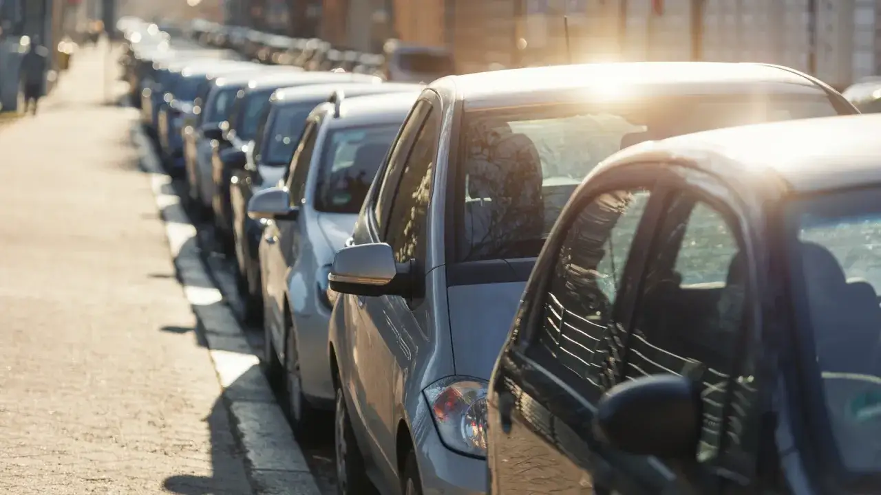 Una hilera de coches aparcados en batería en una calle soleada.