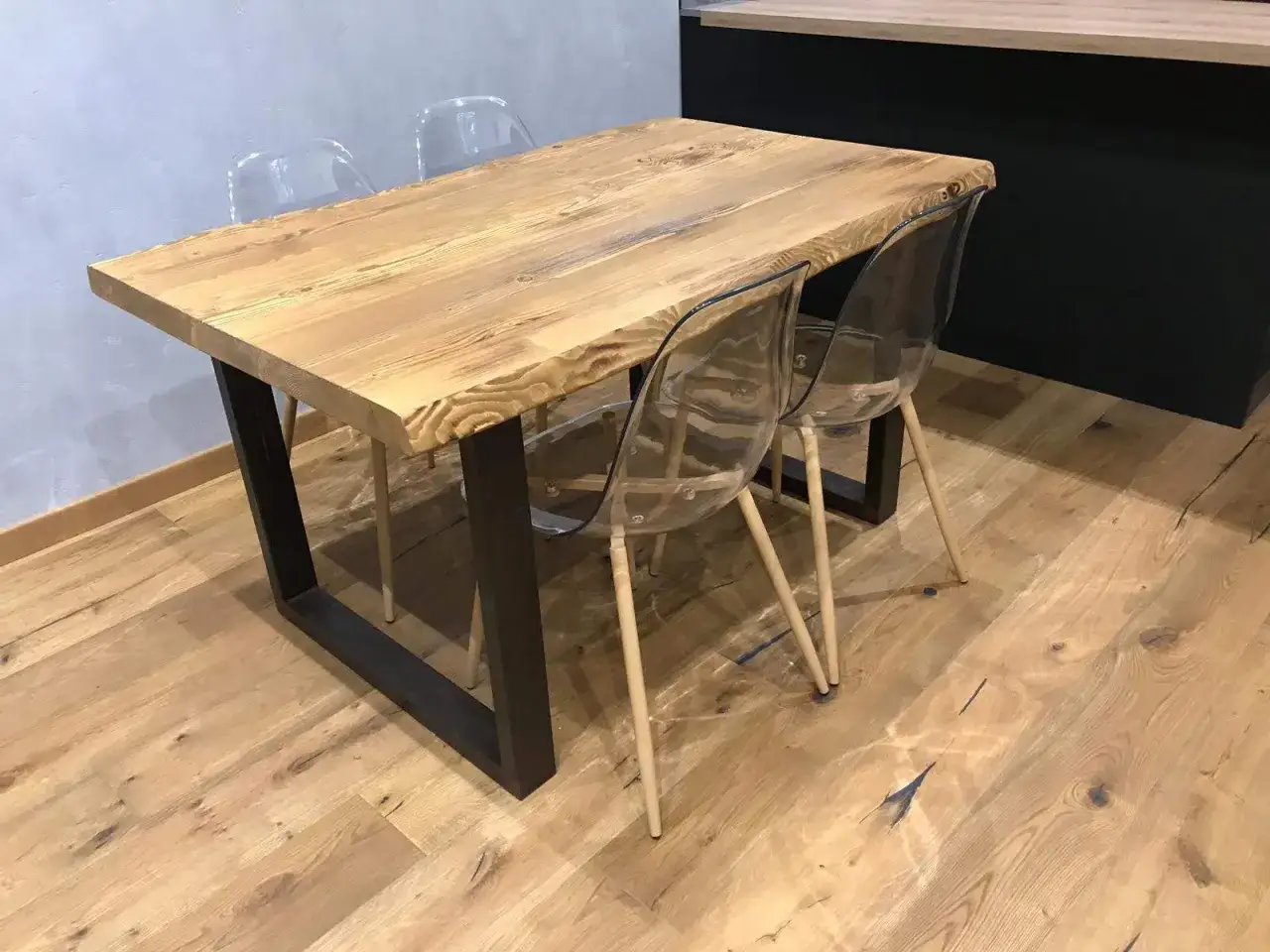Un tavolo in legno grezzo, con gambe in metallo scuro, è un esempio di come costruire un tavolo in legno rustico. Le sedie trasparenti creano un contrasto moderno.