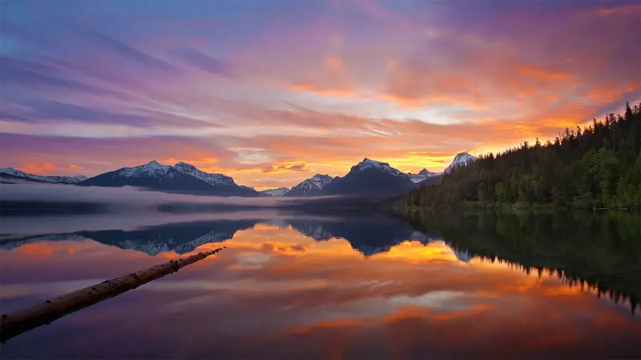 A serene lake reflects a vibrant sunset over snow-capped mountains. This scene inspires how to slow down and relax, finding peace in nature's beauty.