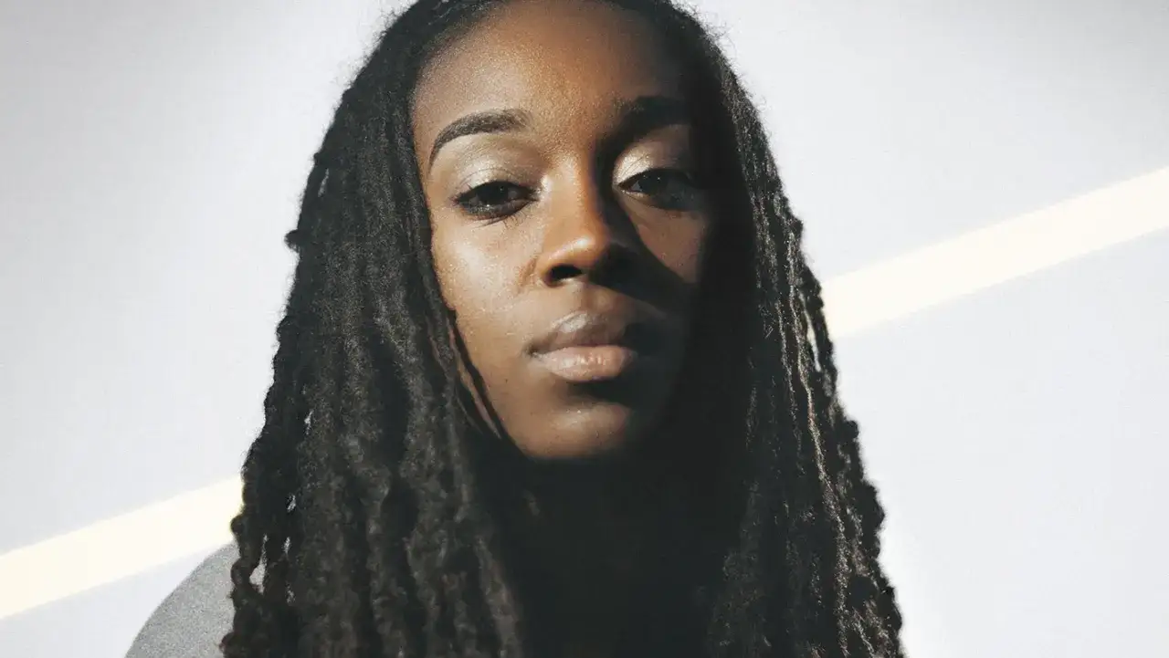 Jackie Hill Perry mit Dreadlocks und nachdenklichem Blick vor hellem Hintergrund.