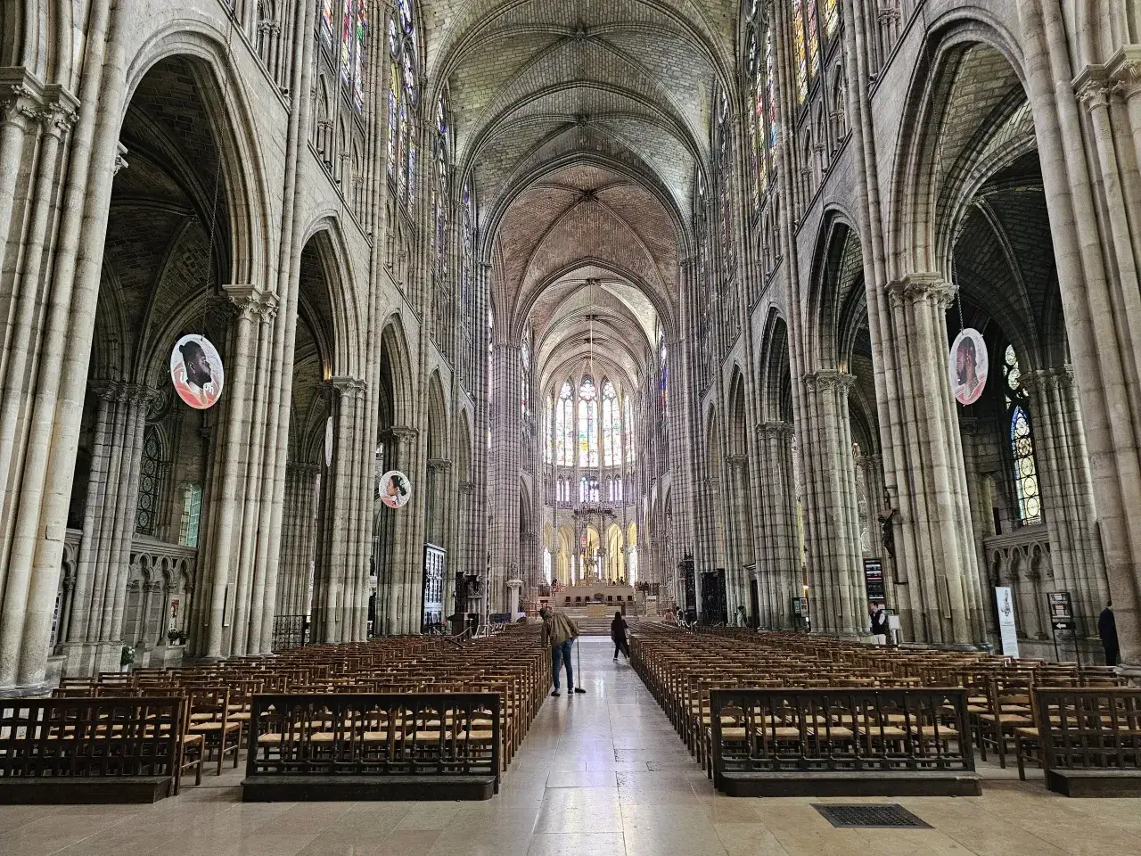 Wnętrze bazyliki Saint-Denis z rzędami drewnianych krzeseł i witrażami.