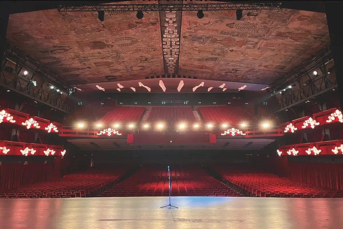 Palco vuoto con microfono, poltrone rosse e soffitto affrescato. Pronto per un cantante ligure.