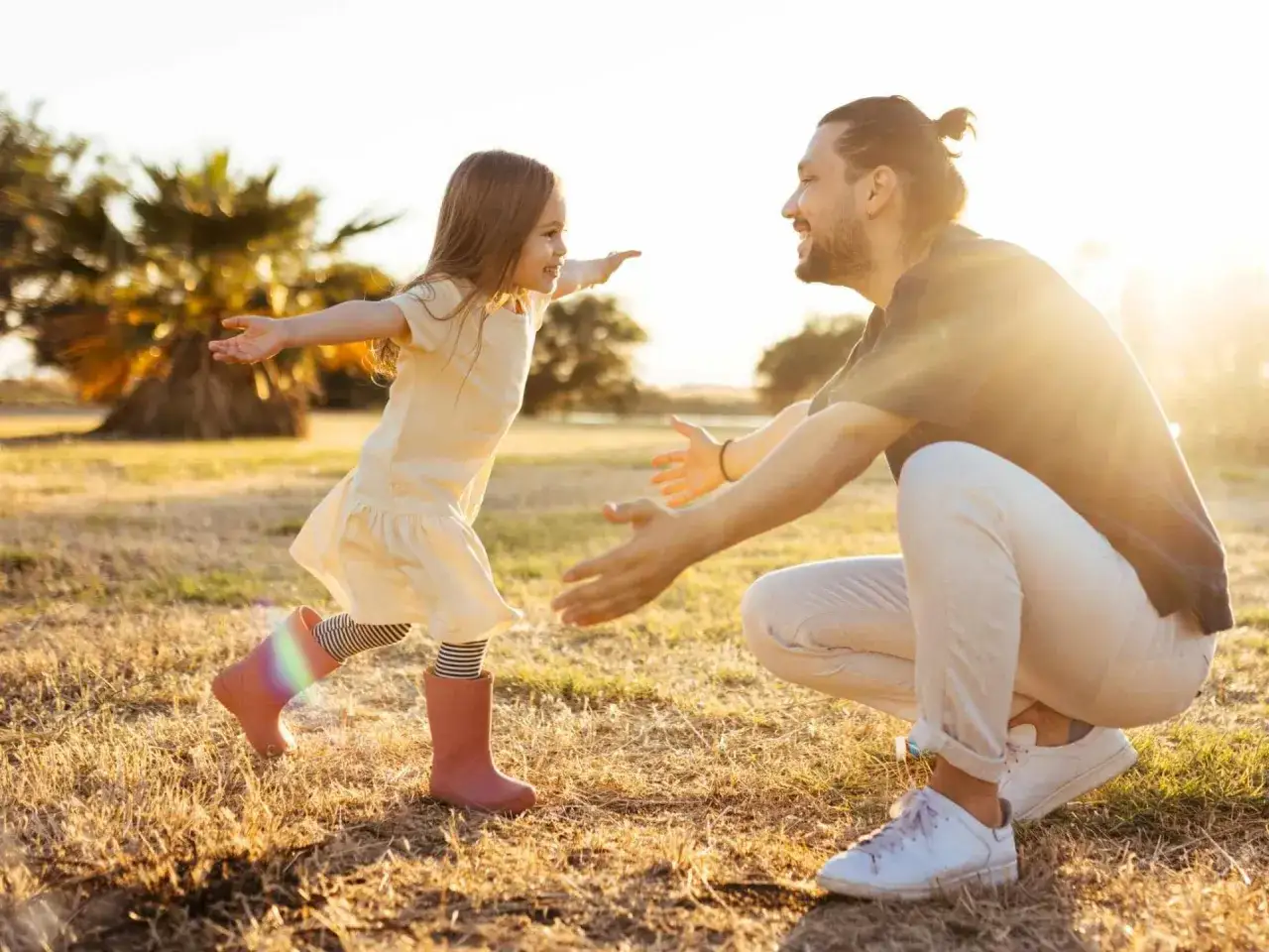 Ein kleines M&auml;dchen rennt mit ausgestreckten Armen auf ihren lachenden Vater zu. Die warme Sonne und die Natur spiegeln die liebevolle vater tochter beziehung wider.