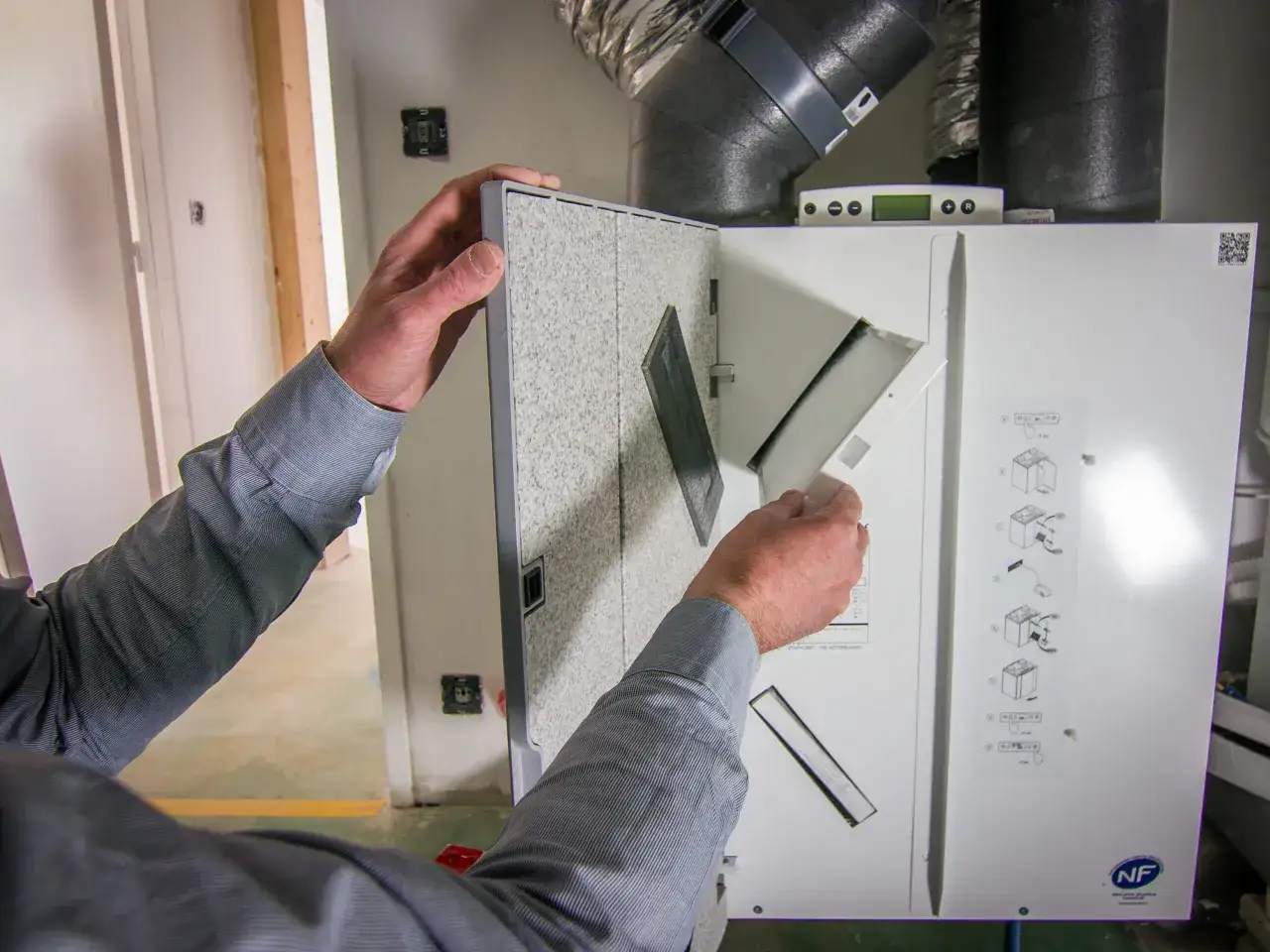 Un technicien effectue l'entretien d'une VMC double flux, vérifiant le filtre et les conduits pour assurer une bonne ventilation.