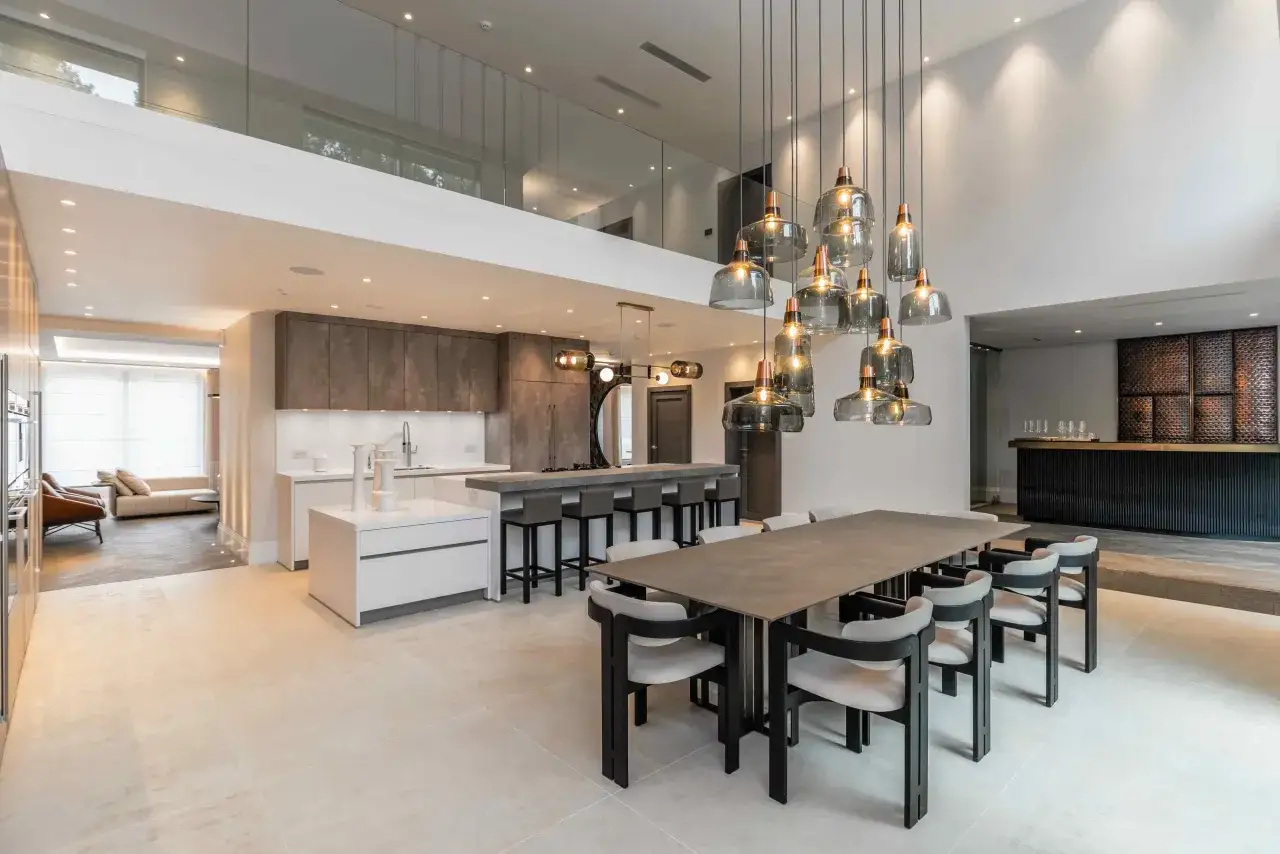 Modern open-plan living space with a large dining table and chairs, a kitchen island with bar stools, and a bar area. The question of whether bar stools should match dining chairs is answered by this stylish design.