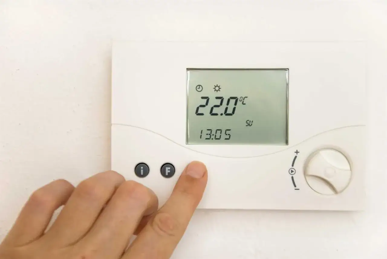 Digitale Heizungssteuerung zeigt 22°C an. Eine Hand drückt einen Knopf. Ab wann heizen?