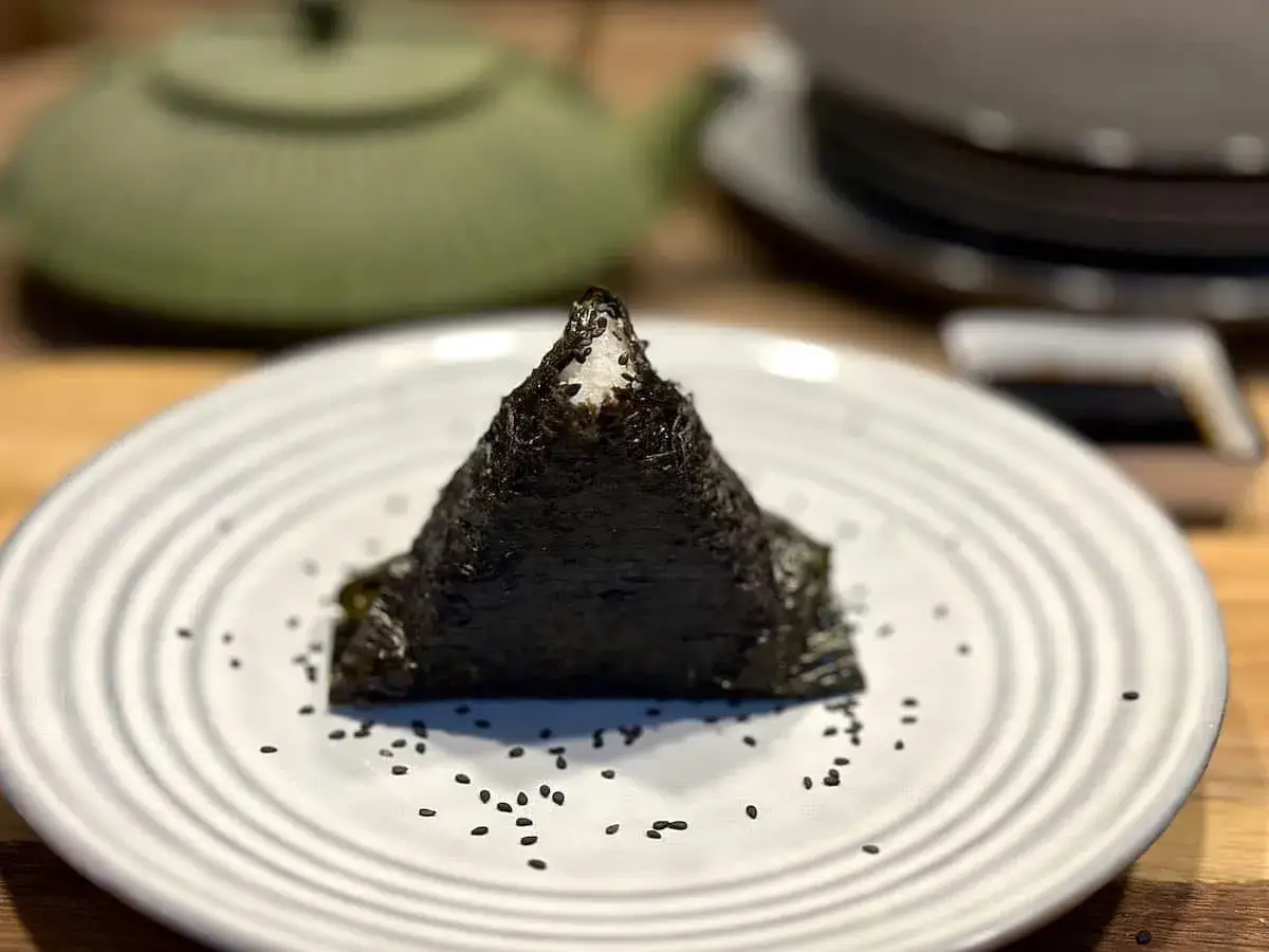 Tr&oacute;jkątne onigiri z tuńczykiem, owinięte w nori, na talerzu z sezamem.