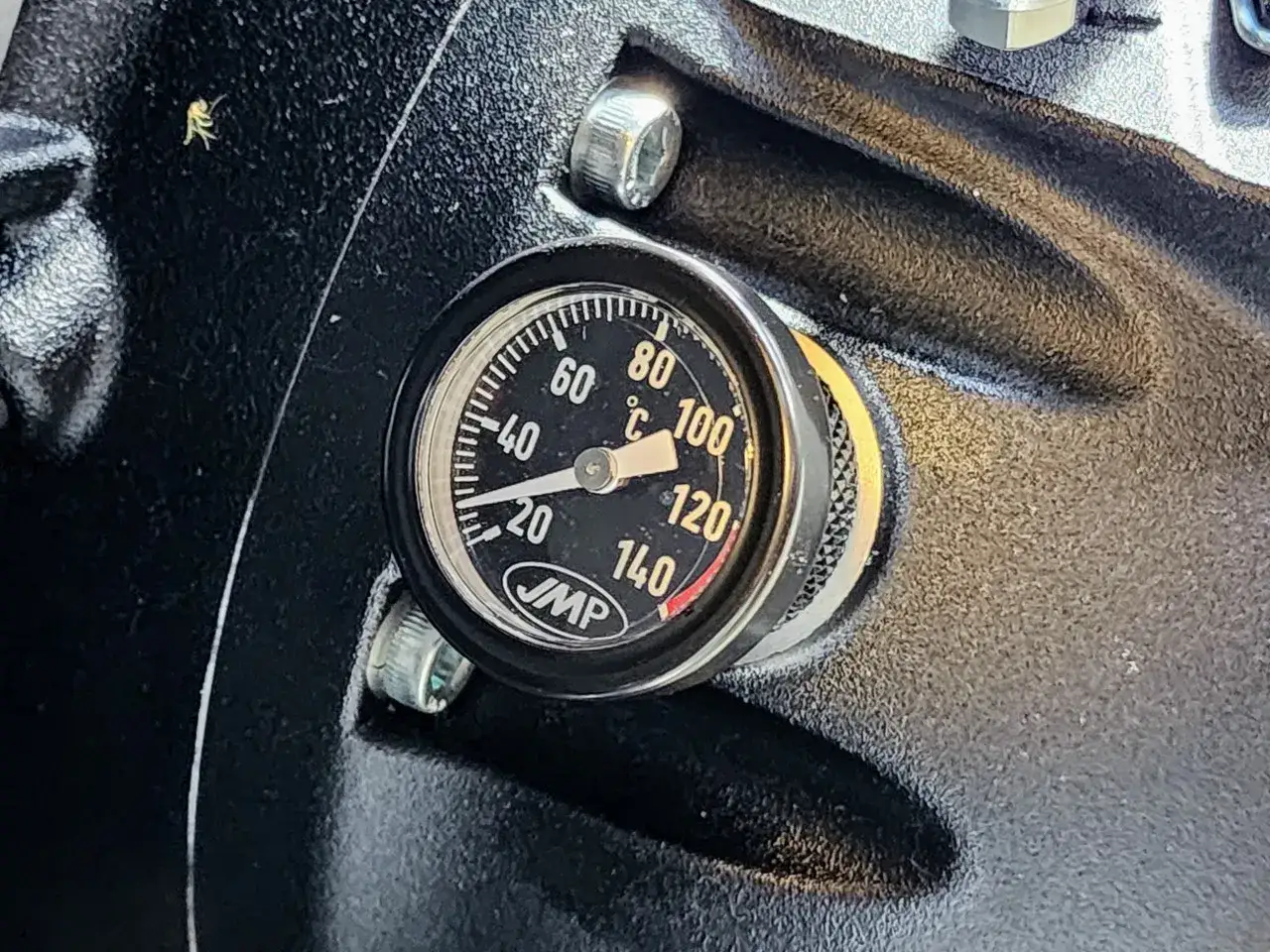 Medidor de temperatura aceite coche JMP, marcando unos 40°C. Un pequeño insecto reposa en la superficie negra.