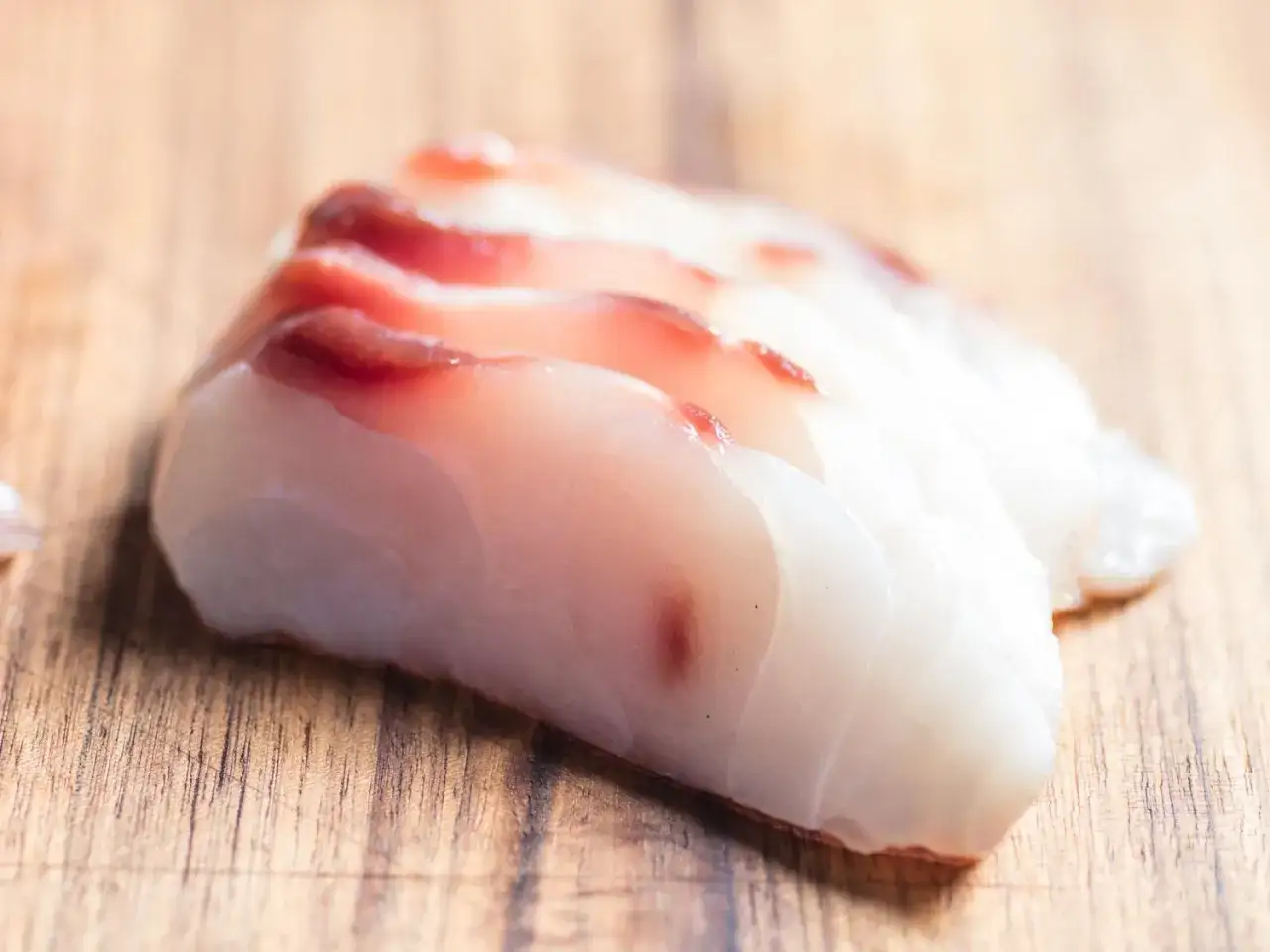 Świeże plastry ryby do sushi, z delikatnym różowym odcieniem, ułożone na drewnianej desce.