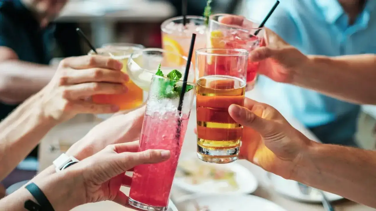 Grupa przyjaciół wznosi toast kolorowymi drinkami. Wśród nich widać wino z sokiem, idealne na letnie popołudnie.