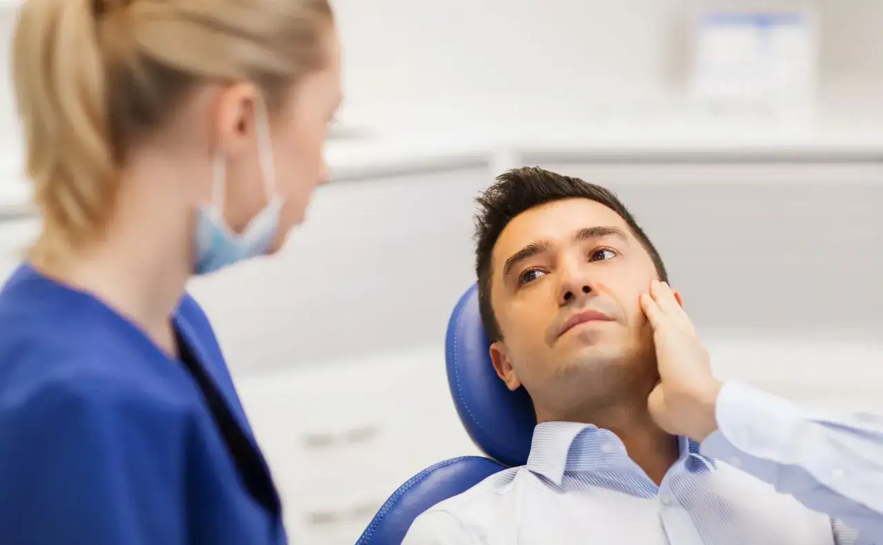 Pacjent u dentysty zastanawia się, ile trzyma znieczulenie. Lekarka w maseczce patrzy na niego z troską.