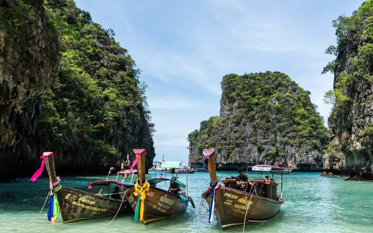Trzy łodzie z kolorowymi wstążkami kołyszą się na turkusowej wodzie między skalistymi wyspami Phuket.
