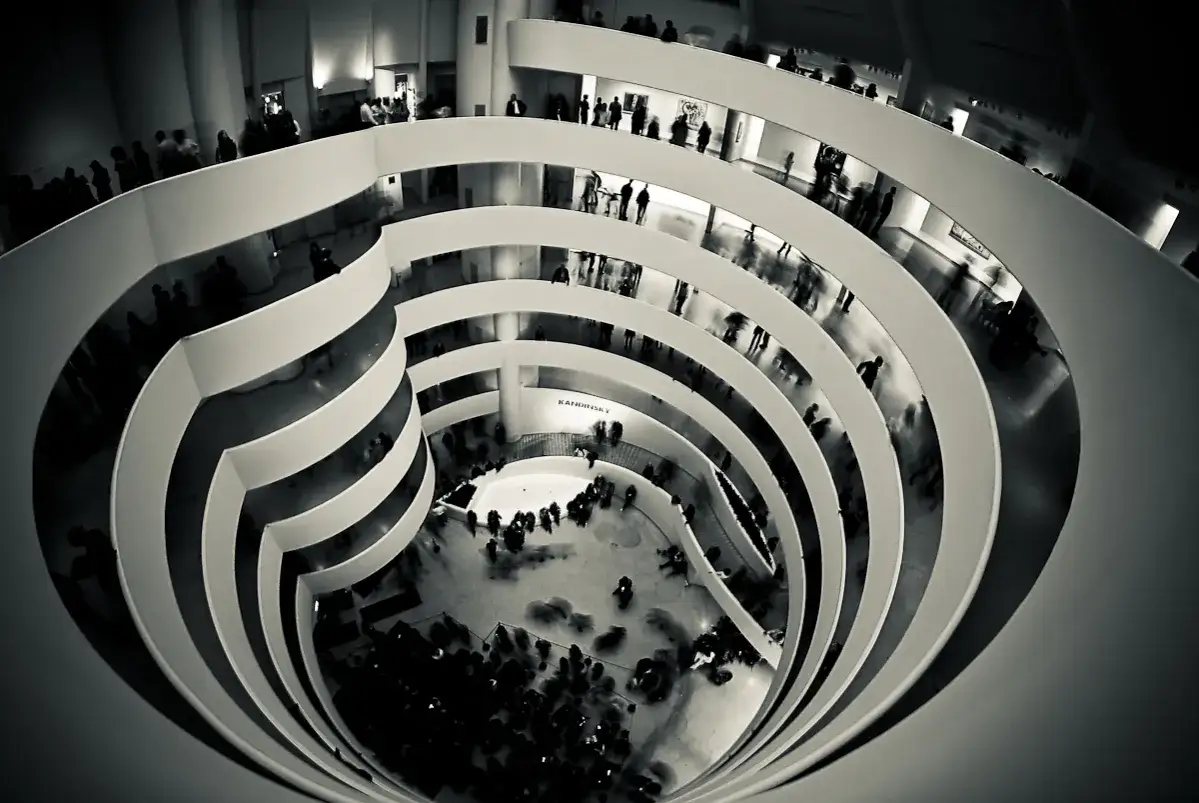 Wnętrze muzeum Guggenheima w Nowym Jorku, gdzie zwiedzający podziwiają dzieła sztuki na spiralnych rampach.