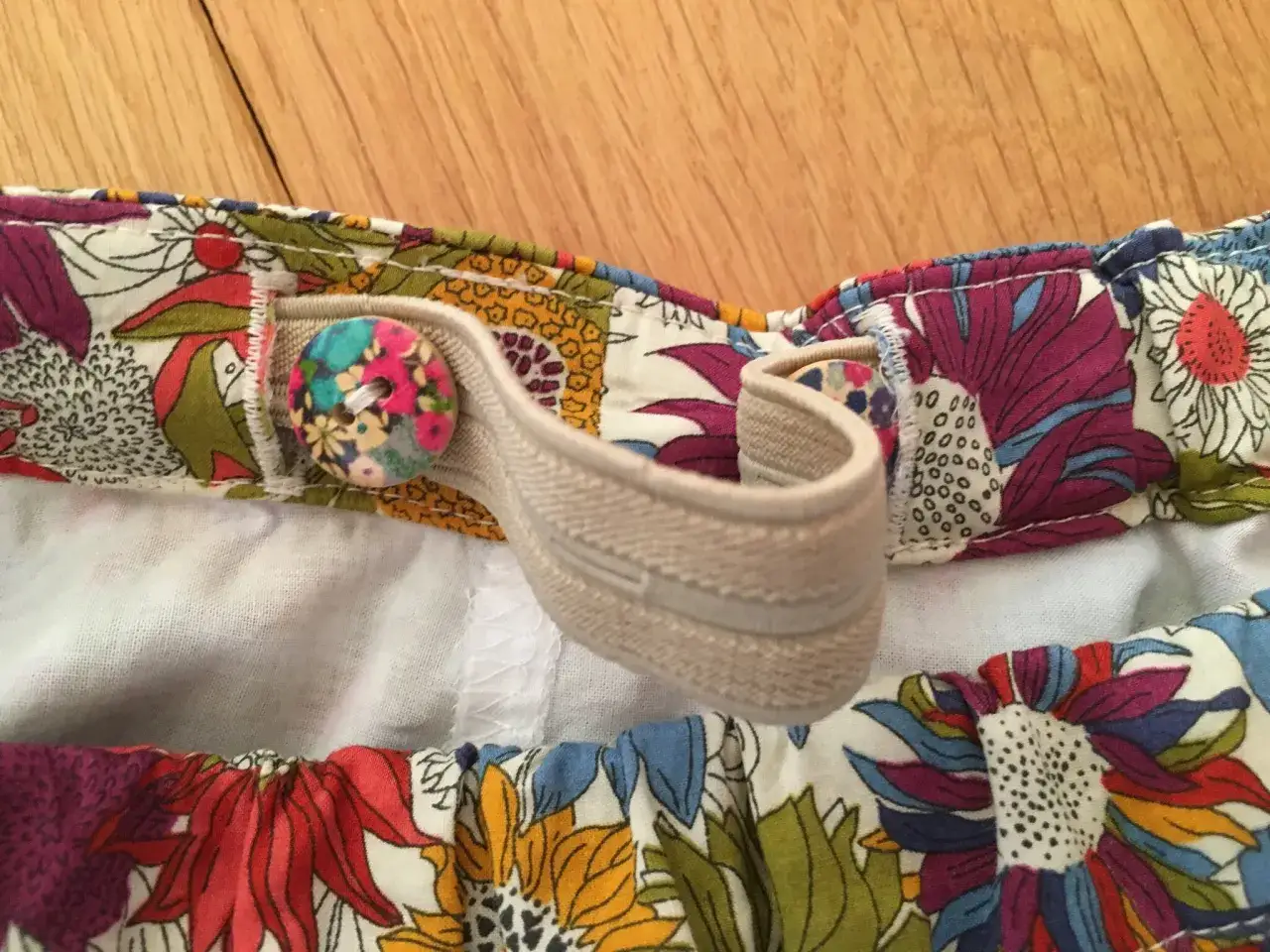 D&eacute;tail d'un pantalon enfant avec un &eacute;lastique boutonni&egrave;re et des boutons fleuris sur un tissu color&eacute;.