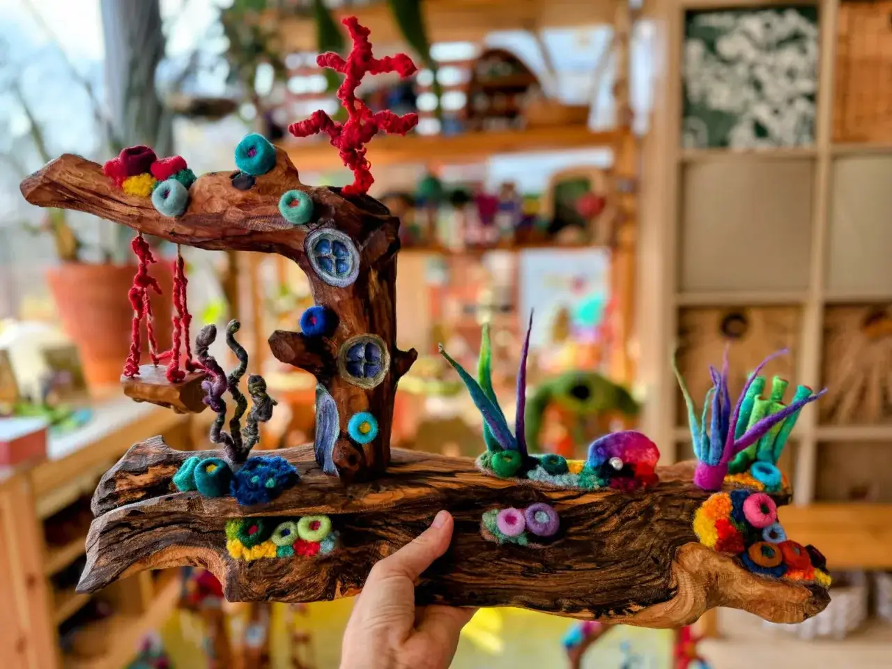 Un tronco de madera transformado en un mundo mágico con **juguetes Waldorf caseros**. Corales, columpios y pequeñas casas adornan esta pieza única.