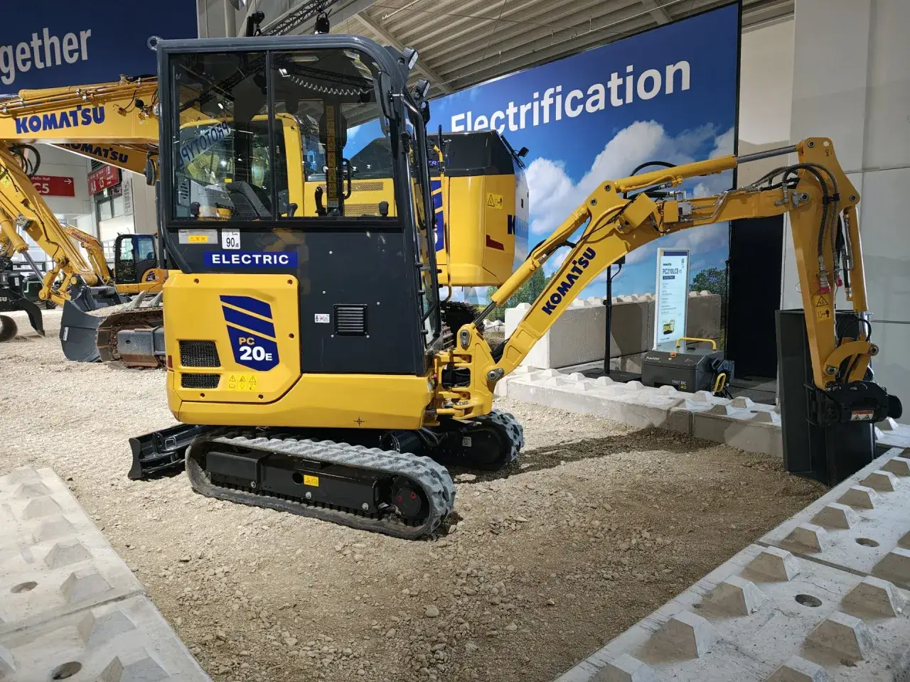 Żółta, elektryczna mini koparka Komatsu PC20E z gąsienicami stoi na placu budowy.