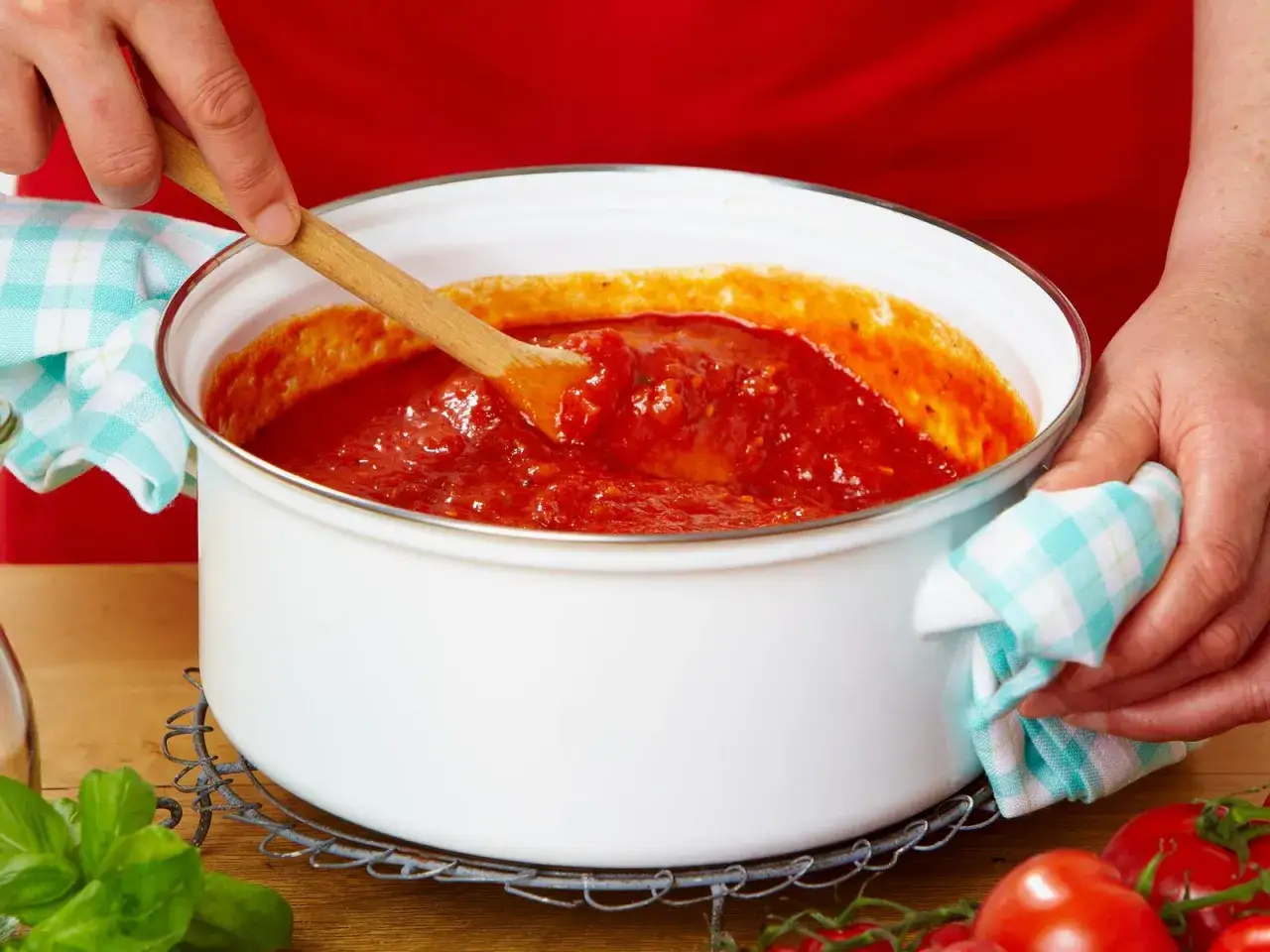 Eine Person rührt mit einem Holzlöffel in einem Topf mit köstlicher Tomatensauce. So einfach ist es, Tomatensauce selber machen!