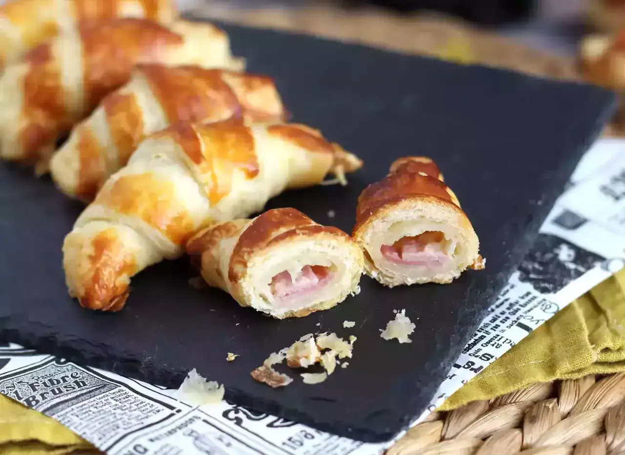 Croissants dorés et feuilletés, certains entiers, d'autres coupés pour révéler leur garniture de jambon savoureuse. Un délice pour le petit-déjeuner ou une pause gourmande.