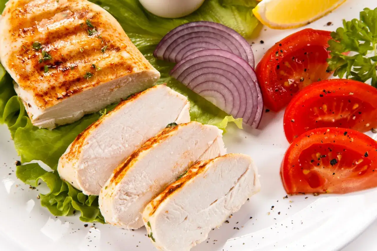 Petto di pollo grigliato affettato, servito con lattuga, pomodoro, cipolla rossa e limone. Un'idea su come condire l'affettato di pollo per un pasto leggero e gustoso.