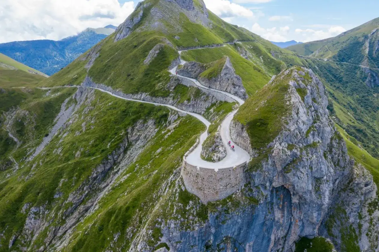 Serpeggiante strada sterrata, la via del sale piemonte, si inerpica su un monte verdeggiante, con ciclisti che affrontano i tornanti.