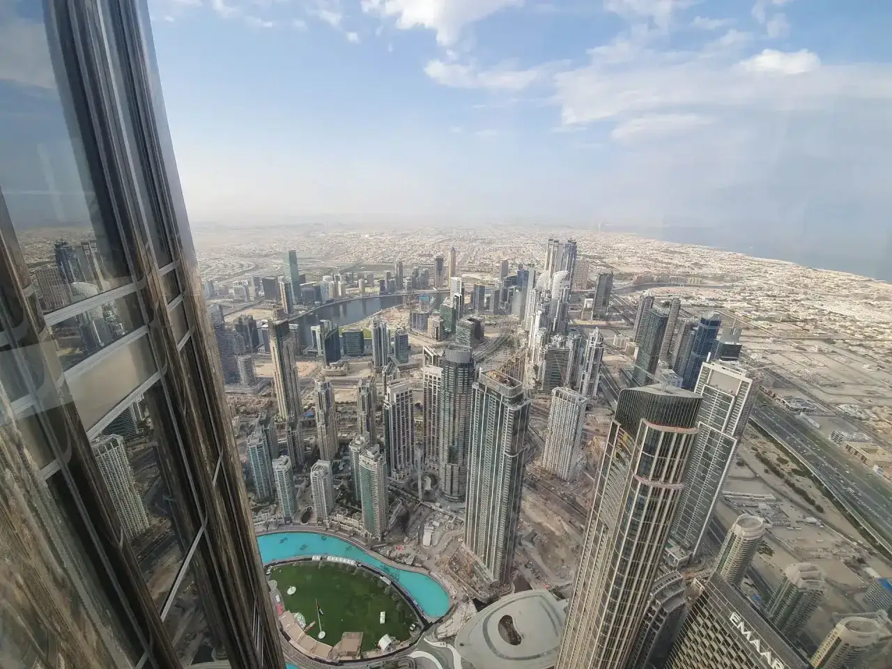 Widok z góry na Dubaj, z dominującym Burj Khalifa. Widać nowoczesne drapacze chmur, jezioro i pustynny krajobraz.