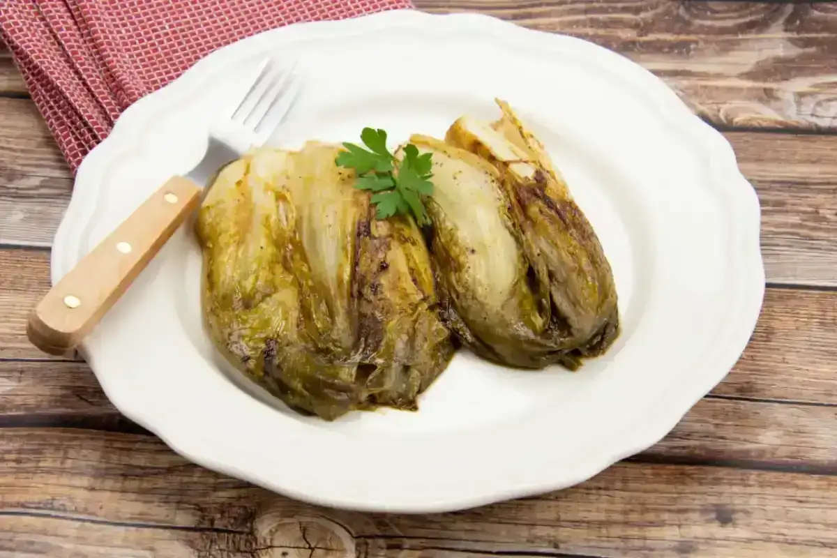 Deux endives caram&eacute;lis&eacute;es &agrave; la po&ecirc;le, garnies de persil, sur une assiette blanche avec une fourchette. Un plat simple et savoureux.