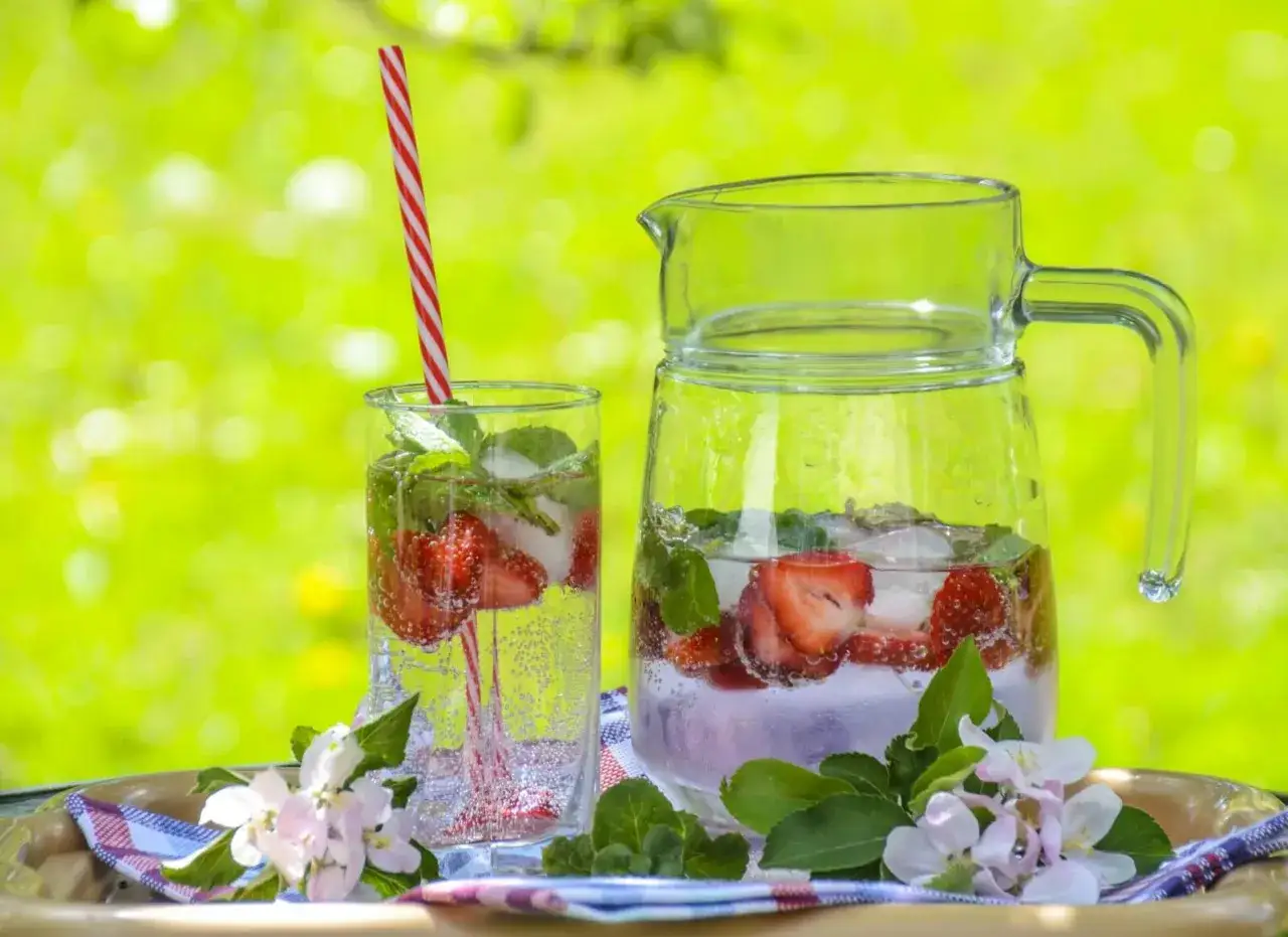 Erfrischendes Erdbeer-Minz-infused Wasser in einem Glas und einer Karaffe, bereit f&uuml;r einen sonnigen Tag im Freien.