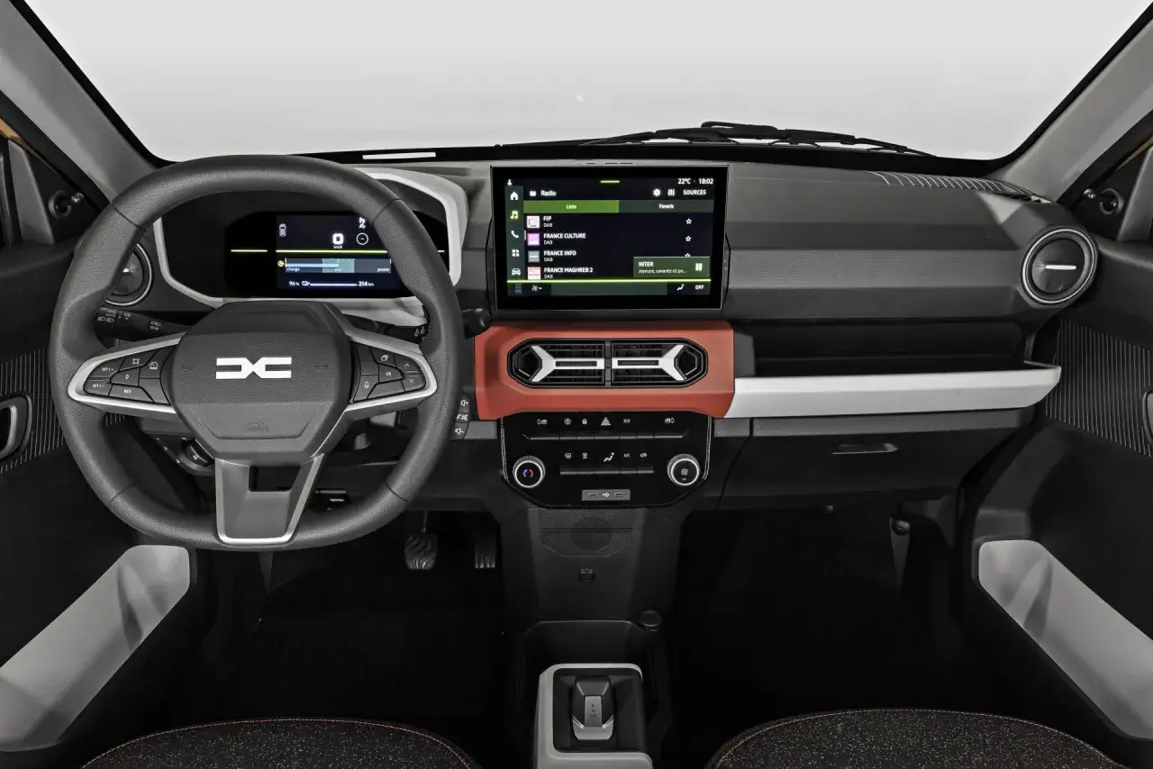 Wnętrze Dacii Spring. Ekran multimediów pokazuje stacje radiowe, a cyfrowy wyświetlacz przed kierowcą informuje o zasięgu. Sprawdź dacia spring cena!