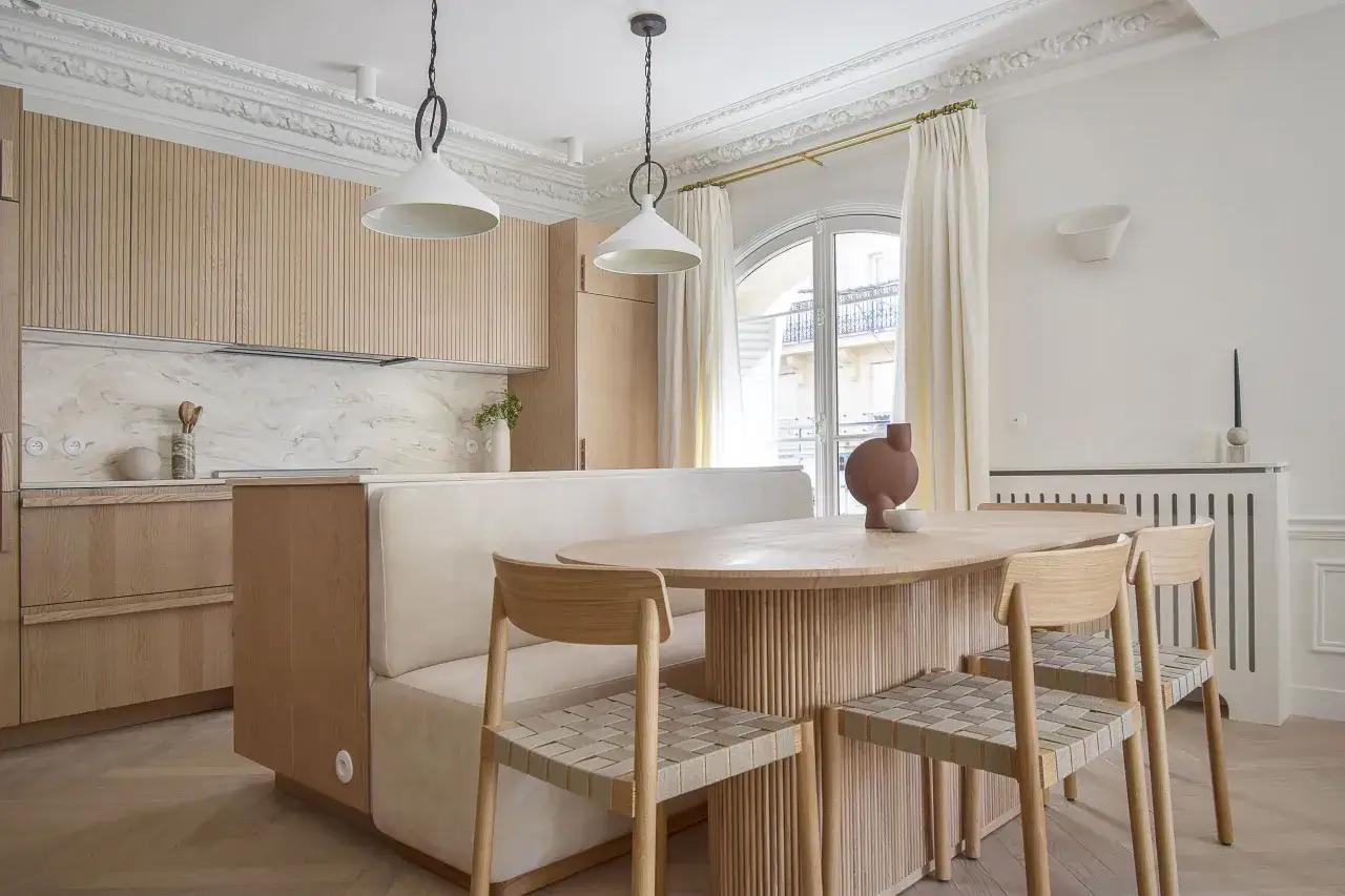 Un &eacute;l&eacute;gant m&eacute;lange travertin et parquet habille cette cuisine-salle &agrave; manger moderne, avec des meubles en bois clair et une banquette confortable.