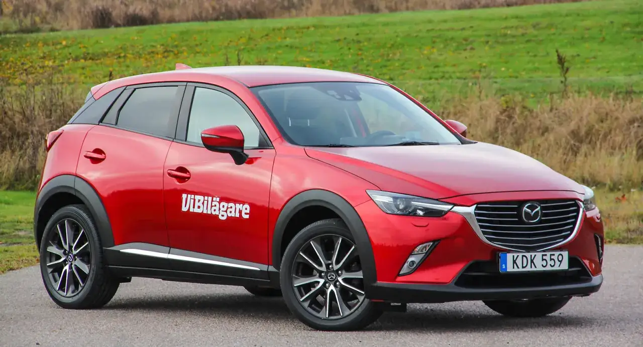 R&ouml;d Mazda CX-3, en begagnad bil som testas. Den st&aring;r parkerad utomhus med en gr&ouml;n kulle i bakgrunden.