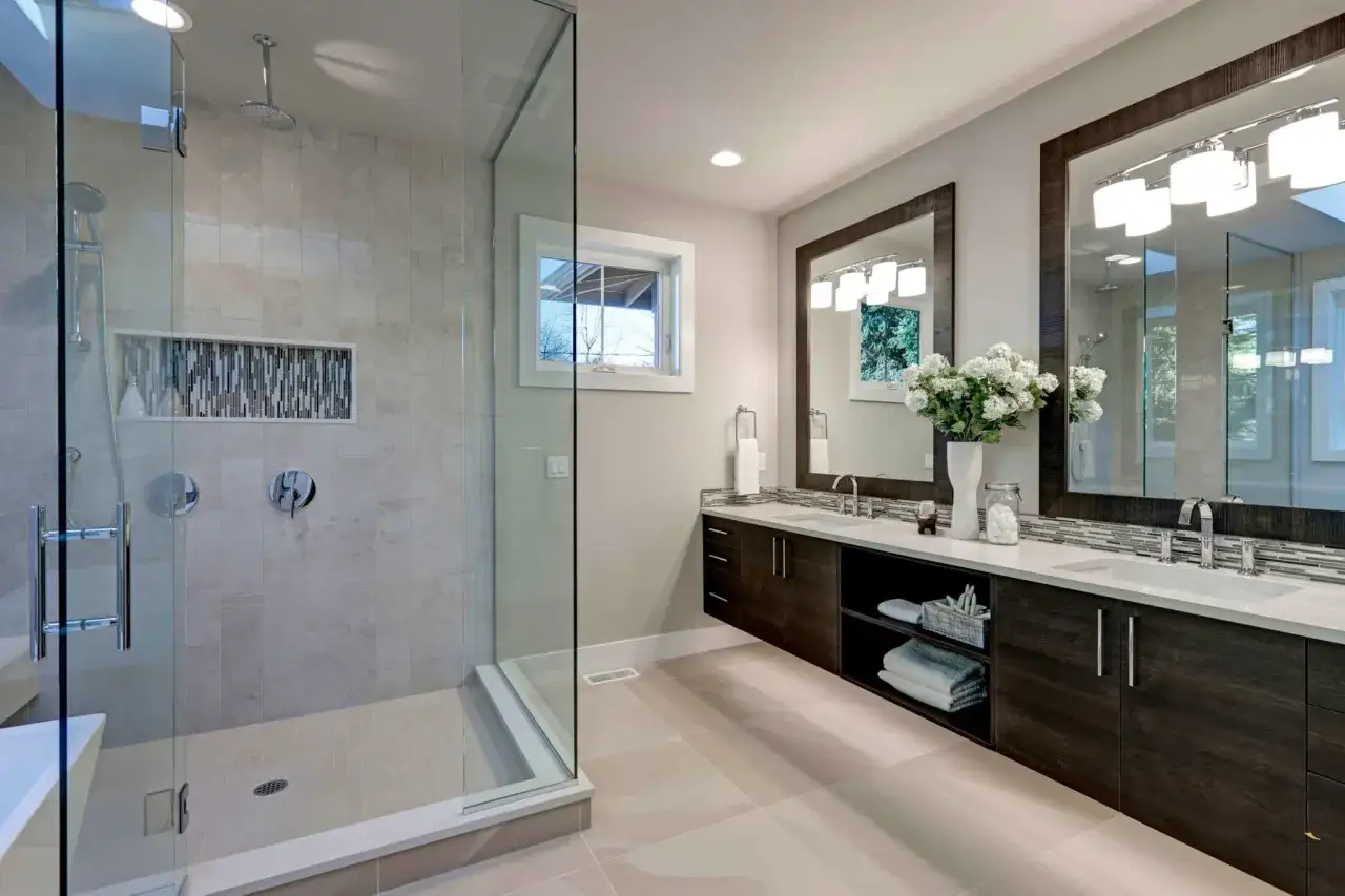 Elegantes baños modernos con ducha de cristal, doble lavabo y armarios oscuros.