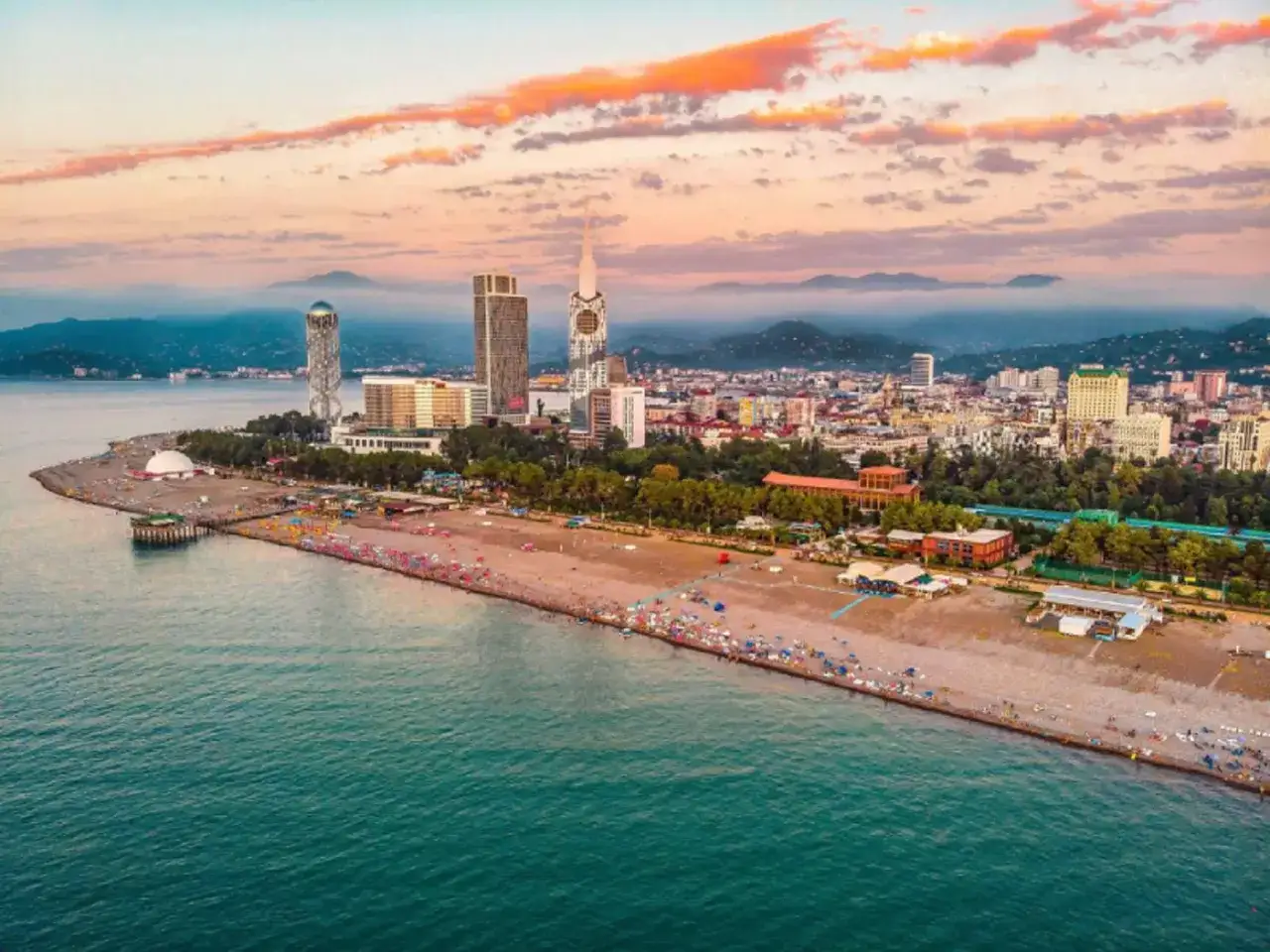 Batumi, Gruzja: tanie wycieczki nad morze. Widok na plażę, nowoczesne budynki i góry o zachodzie słońca.