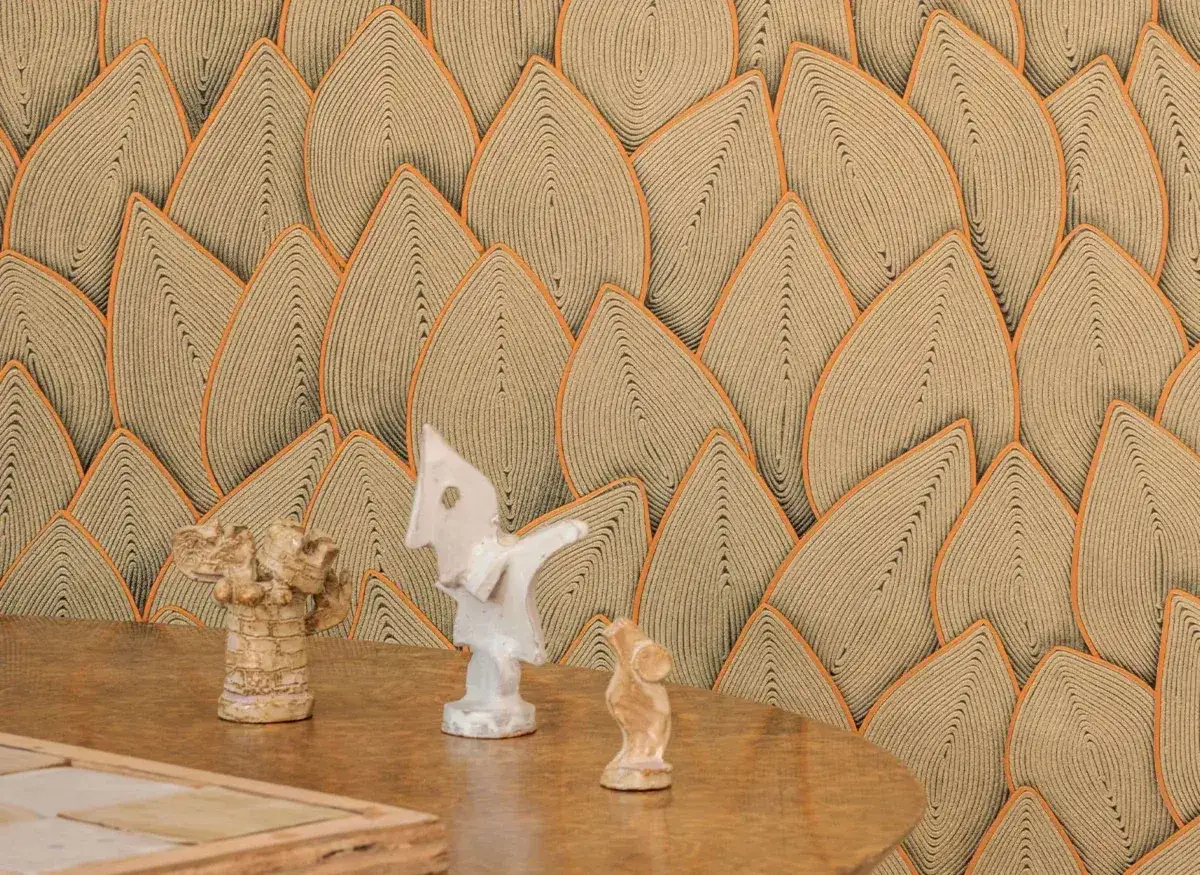 Sur un mur au motif d'applique en forme de feuilles, trois petites sculptures se dressent sur une table en bois.