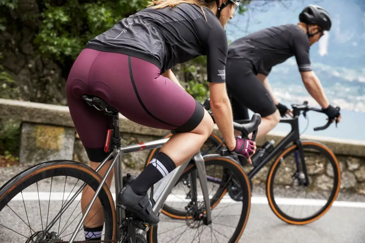Zwei Radfahrerinnen auf einer Bergstraße. Die vordere trägt eine bordeauxrote Radhose, die über einer dünnen Unterhose getragen wird.