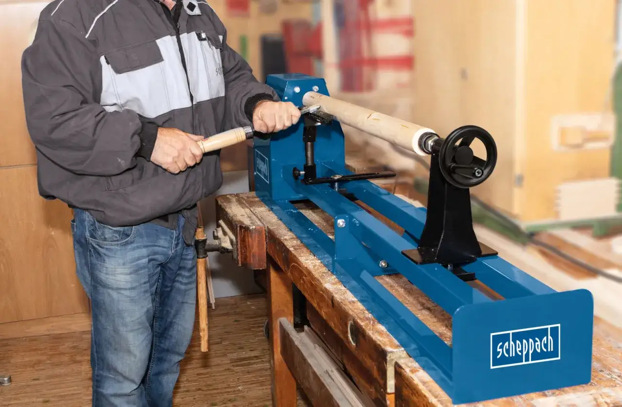 Un artisan utilise un tour à bois bleu de marque Scheppach pour façonner un objet en bois.