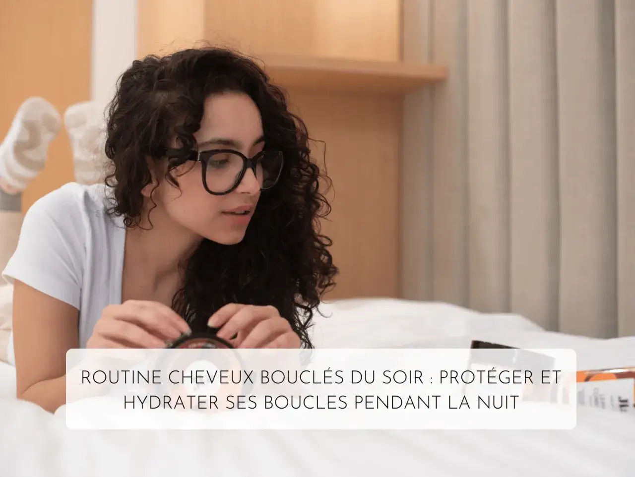 Jeune femme aux cheveux bouclés, lunettes noires, se préparant pour un soin cheveux nuit. Elle tient un pot de crème.