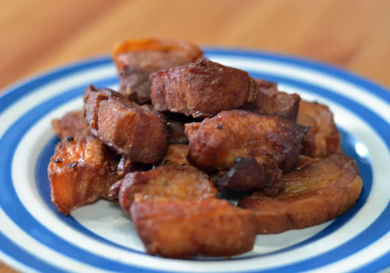 Crispy fried pork belly, or chicharrón, piled high on a blue and white striped plate, ready to be enjoyed.