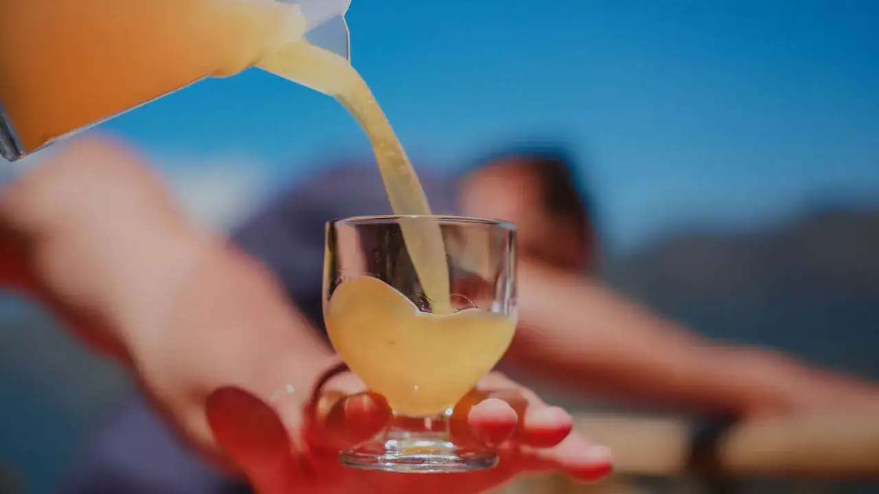 Ein Glas wird mit Poncha Madeira gef&uuml;llt, einem traditionellen Getr&auml;nk von Madeira, im Hintergrund verschwommene Landschaft.