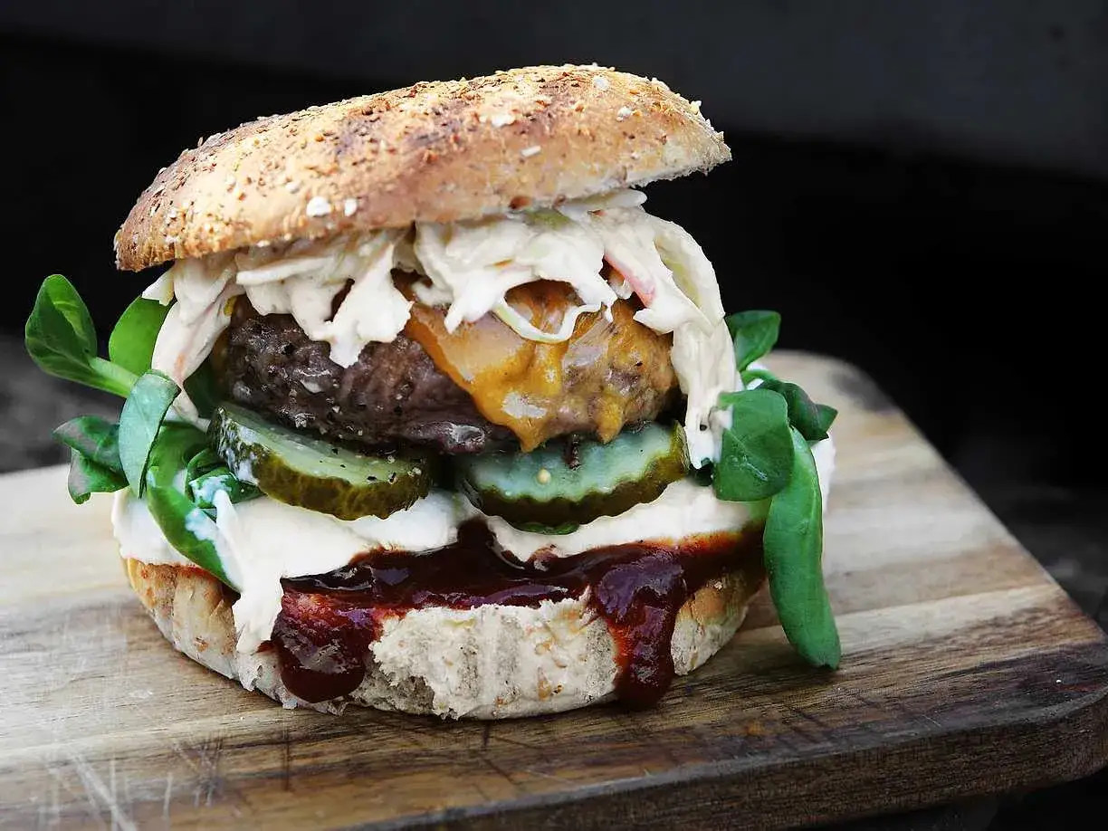 En saftig hamburgare med ost, pickles, kål och en härlig sås på ett grovt bröd.