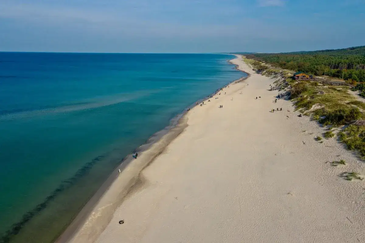 Szeroka, piaszczysta plaża nad Bałtykiem, gdzie ludzie spacerują. To dowód, że Litwa ma dostęp do morza bałtyckiego.