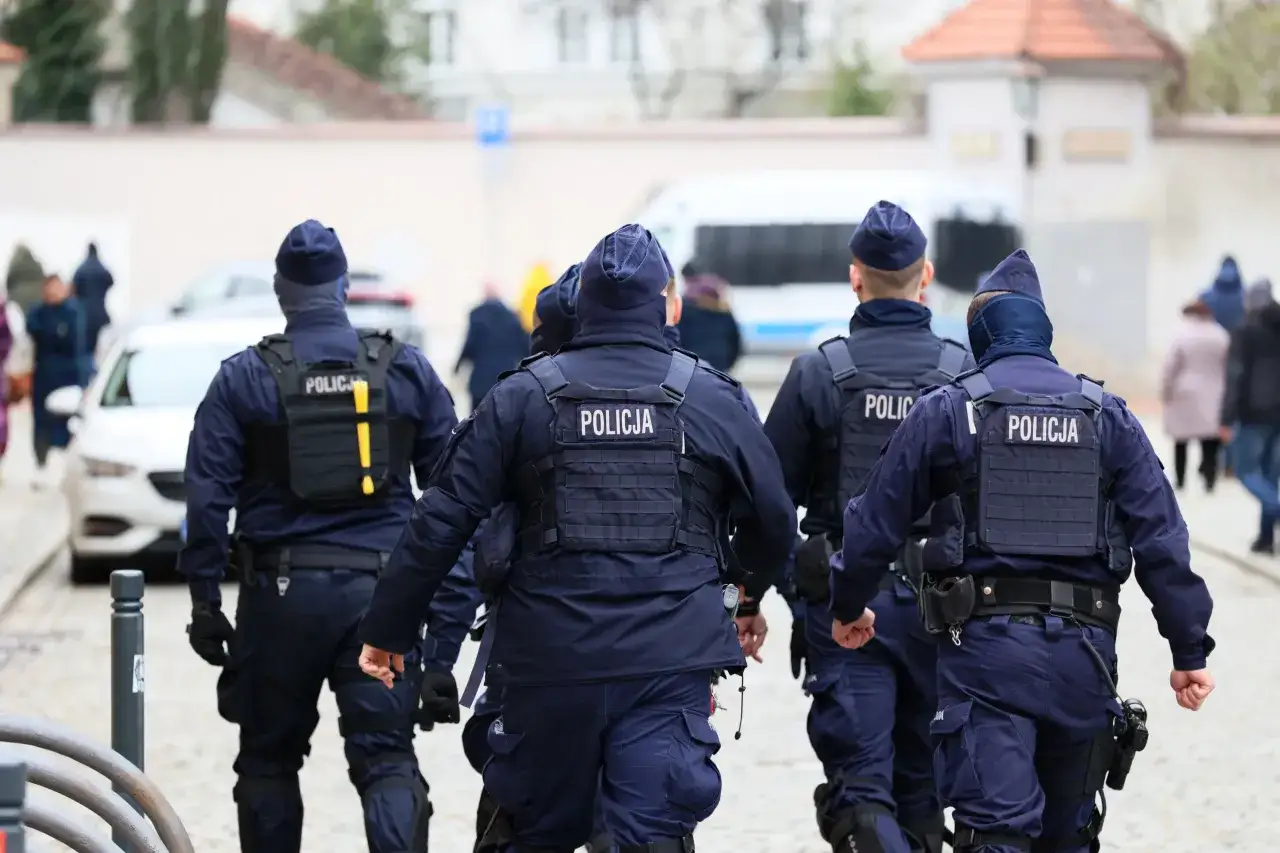 Grupa policjantów w mundurach idzie ulicą. W tle widać budynki i samochody. To obraz, który może przypominać o służbie i przyszłej emeryturze policyjnej.