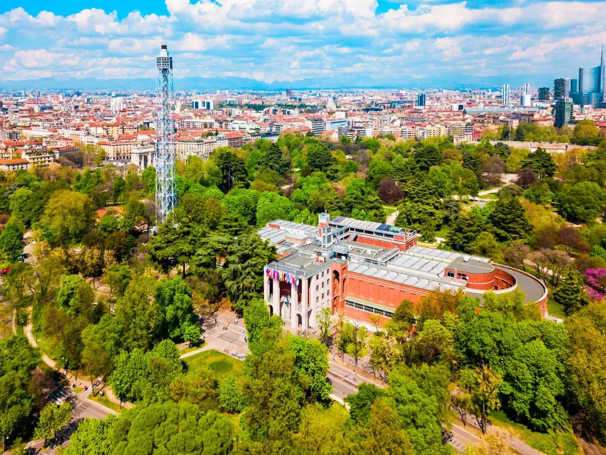 La torre bianca di Milano si erge su un parco lussureggiante, con edifici storici e moderni sullo sfondo.