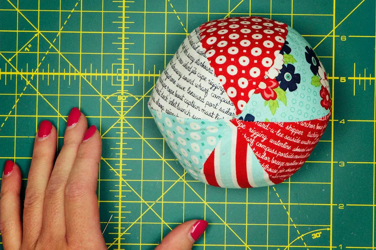 Balle en tissu aux motifs marins, idéale pour un **patron gratuit balle en tissu**. Une main aux ongles vernis rose vif est posée à côté.