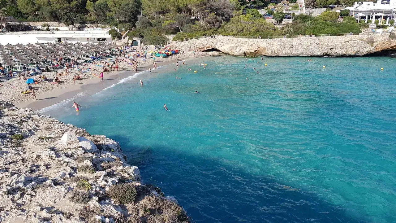 Słoneczny dzień na plaży Cala Domingos. Ludzie opalają się pod parasolami i kąpią w turkusowym morzu.