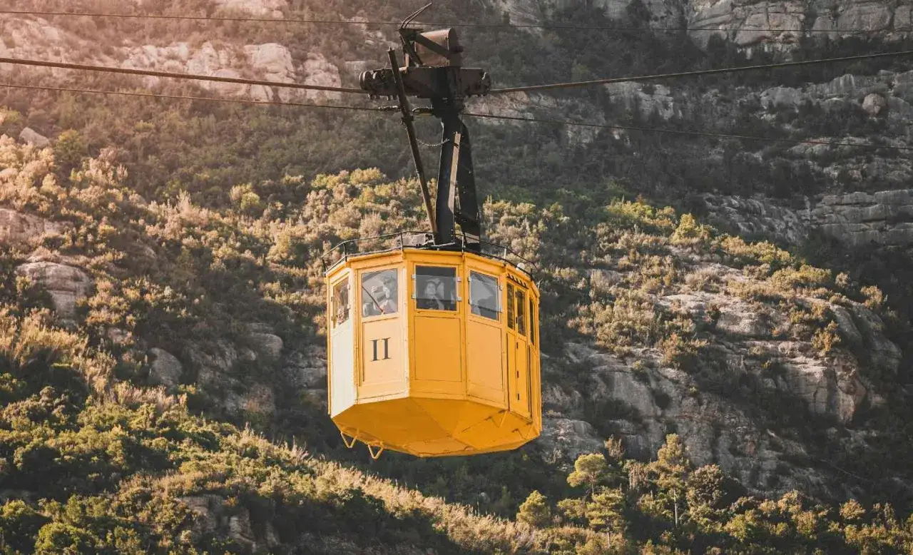 A yellow cable car ascends the rugged slopes of Montserrat. Passengers gaze out the windows as the cable car montserrat travels through the scenic mountain landscape.