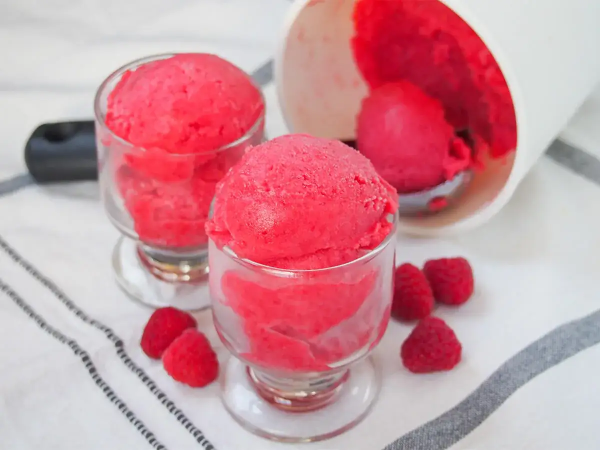 Erfrischendes Himbeersorbet-Rezept: Zwei Gläser gefüllt mit leuchtend rotem Sorbet, daneben frische Himbeeren.